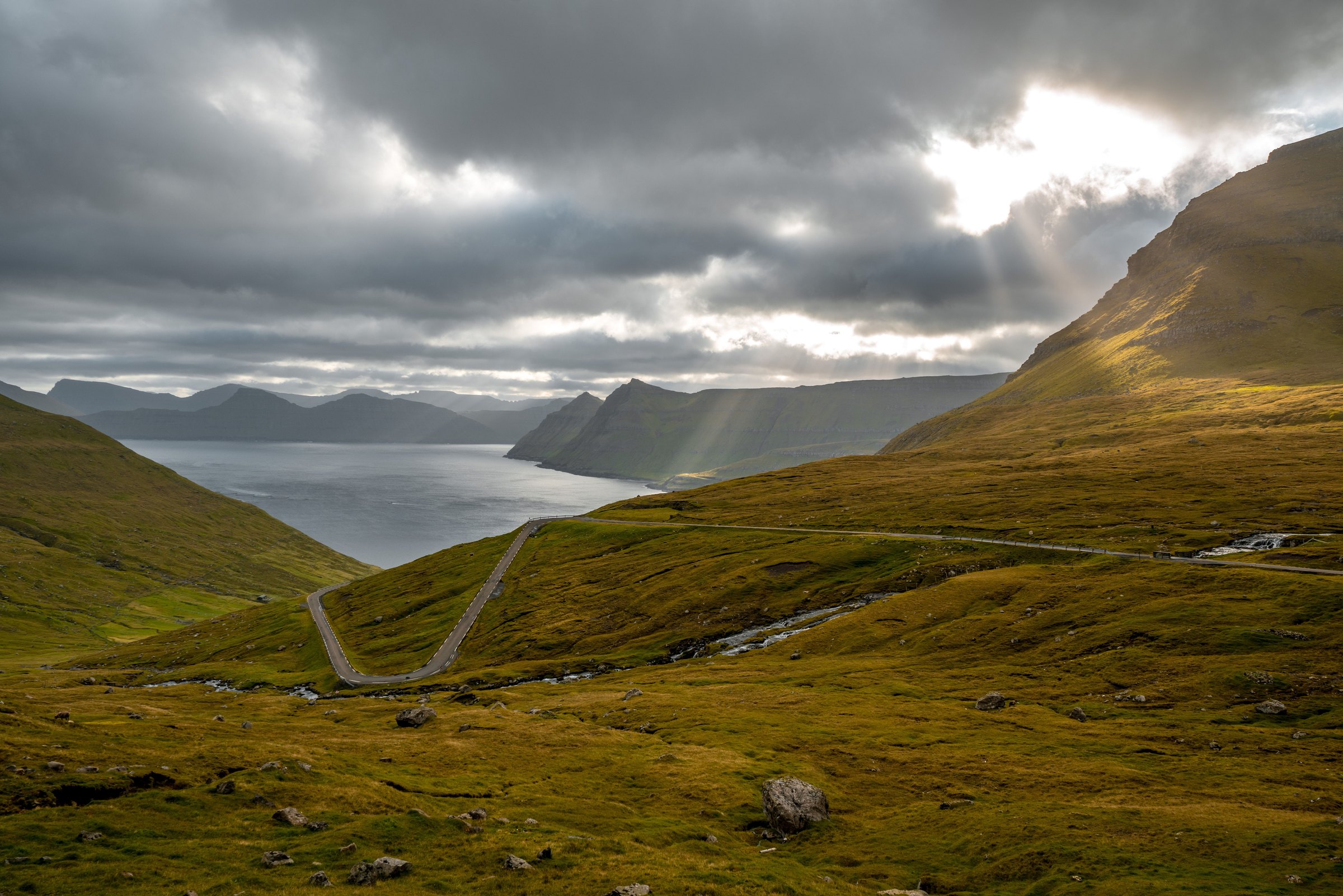 Road winding through green hills above a fjord, Faroe Islands