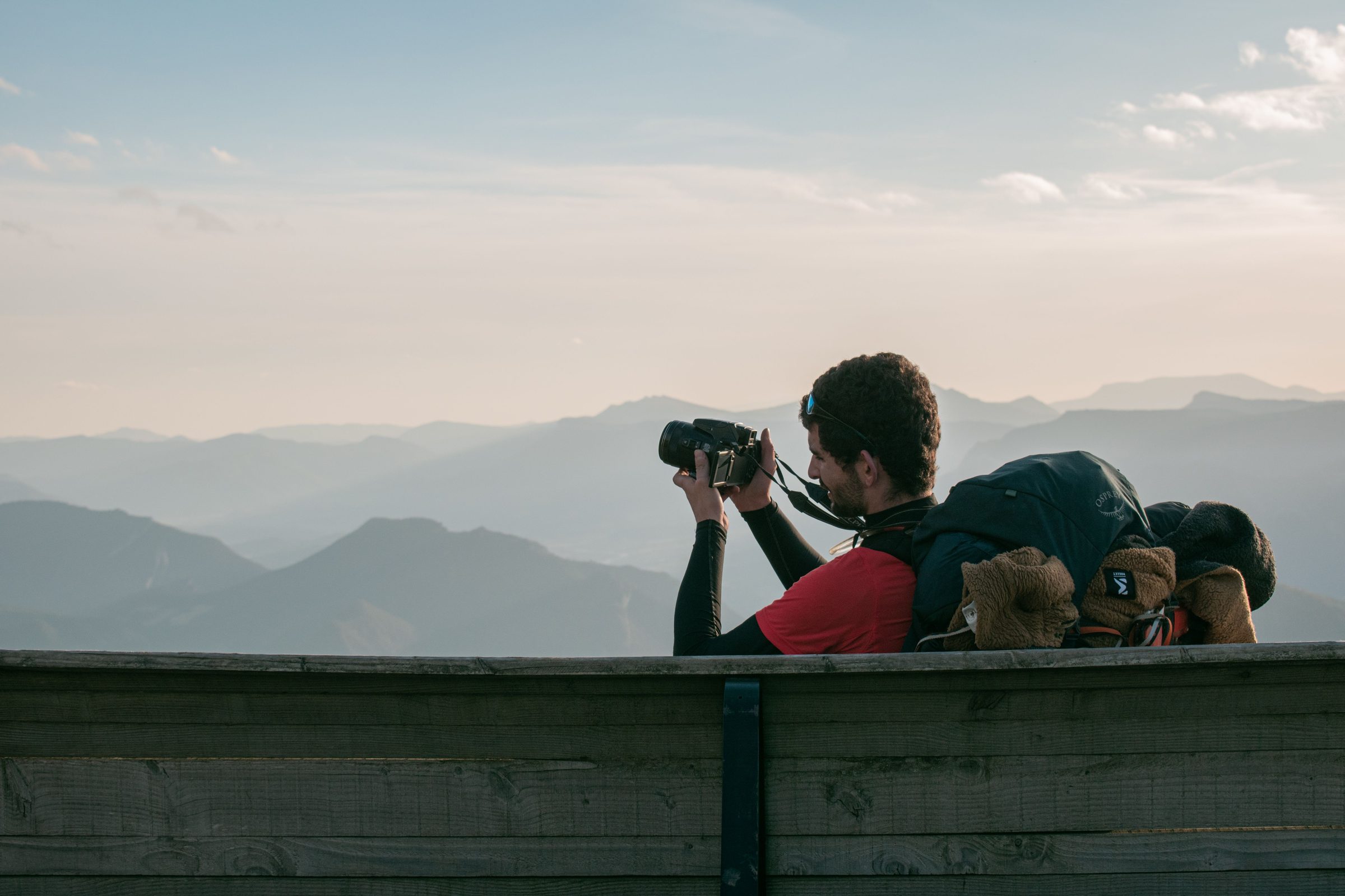 Traveller with a backpack photographing a mountain viewpoint with a mirrorless camera