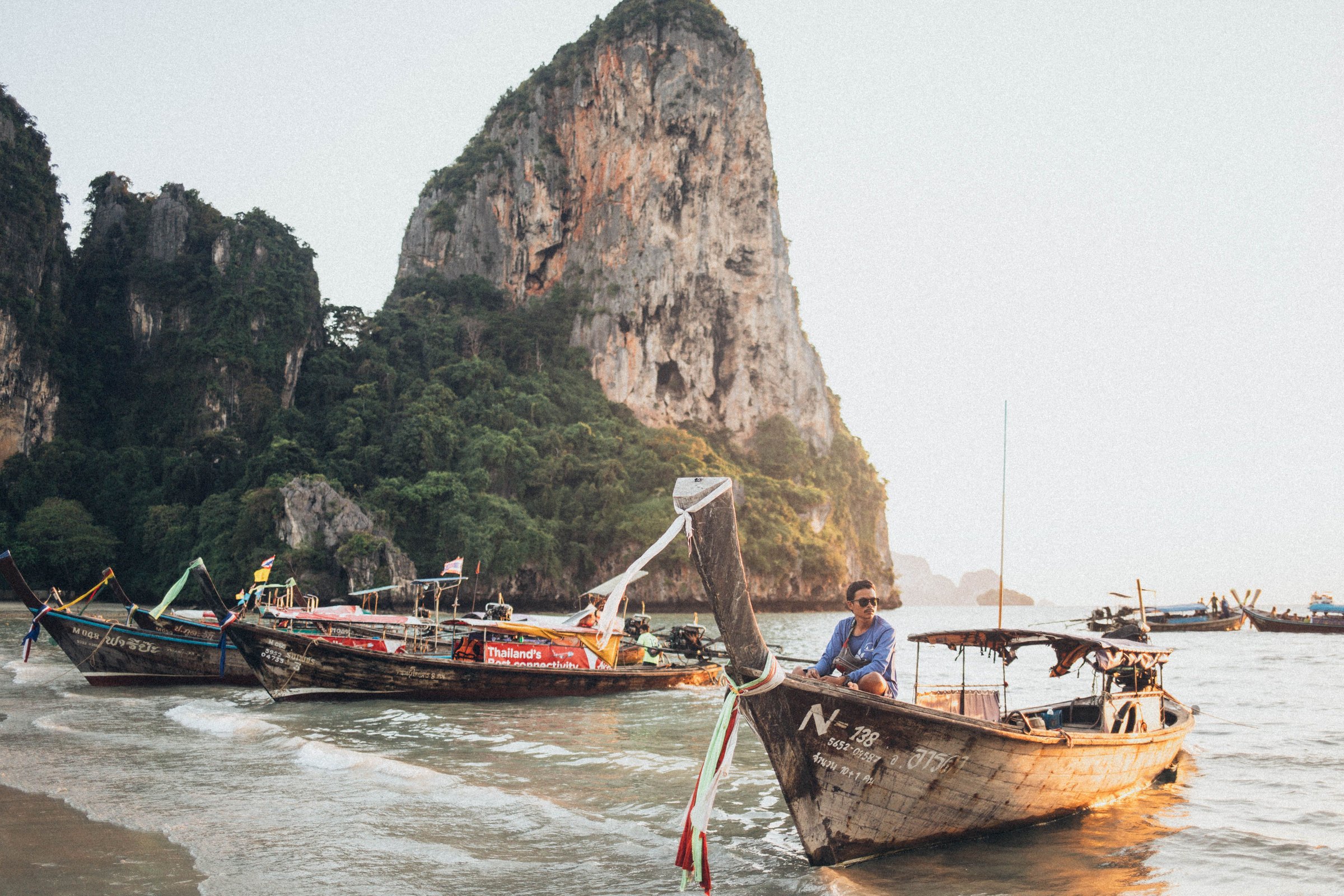Traditional longtail boats moored below limestone cliffs on a Thai beach